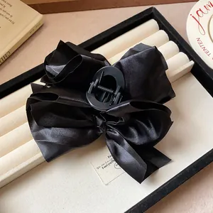 Close-up of a large black fabric bow hair claw clip with satin finish on a display tray.