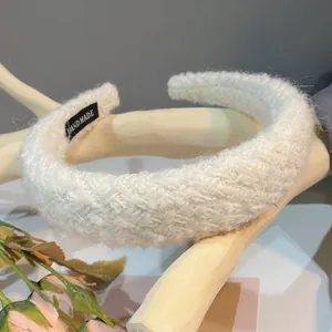 Close-up of white bouclé knit headband featuring a black handmade label on the inner side.