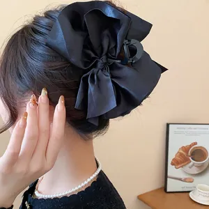 Close-up detail of a large elegant black fabric bow hair claw clip worn by a model