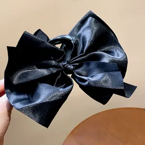 Close-up detail of a large black satin bow shark hair clip with elegant silk texture