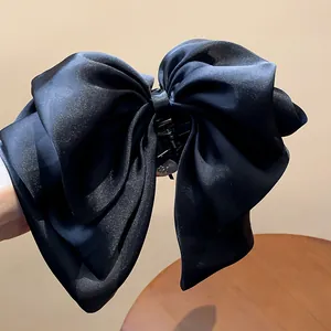 Close-up of a large black fabric bow hair claw clip with a elegant satin texture.