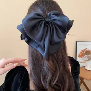 Detail of large black satin bow hair claw clip worn on long wavy brown hair