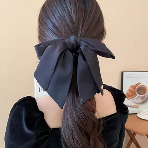Close-up of a large black satin bow hair claw clip styled on long wavy hair from the back.