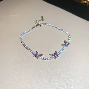 Détail macro d'un bracelet argenté avec zircons étincelants et breloques papillon mauves
