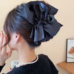 Detailed back view of a large black satin bow hair claw clip on a person's bun.