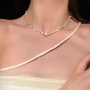Detail view of a silver irregular bead necklace with a central pearl on model's neck.