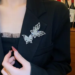 Dettaglio di una scintillante spilla a farfalla traforata con strass su un blazer nero raffinato.