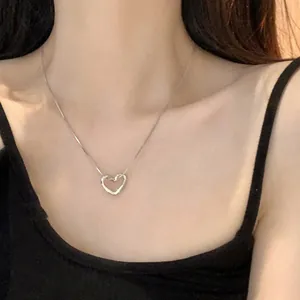 Macro view of a minimalist silver hollow heart pendant necklace worn on a woman's neck.