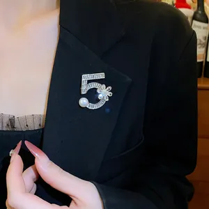 Dettaglio di una spilla numero 5 scintillante con perle su un blazer nero