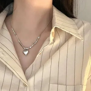Close-up view of an elegant silver heart pendant necklace worn with a striped shirt