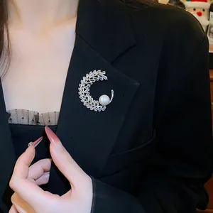 Primo piano di una spilla a mezzaluna con strass e perla bianca su un blazer nero.
