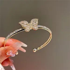 Close-up of sparkling zircon butterfly charm on gold-plated open bangle bracelet