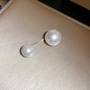 Primo piano di una spilla minimalista con doppia perla e barra dorata su fondo champagne
