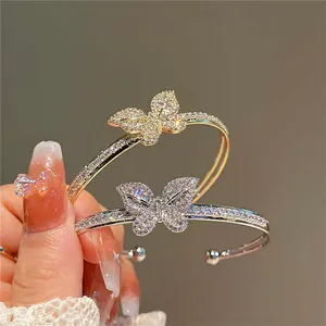 Macro detail of zircon-encrusted butterfly motif on gold and silver open bangles