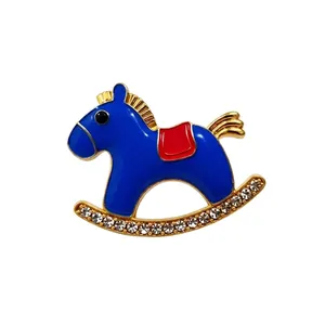 Blue enamel rocking horse brooch with rhinestones and red saddle in gold finish.
