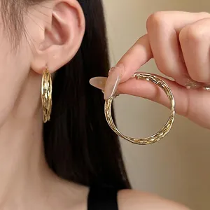 Elegant gold geometric hoop earrings with textured finish on an Asian model