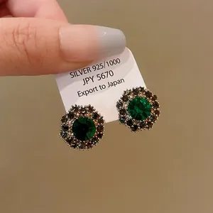 Dettaglio di eleganti orecchini a lobo a fiore verde smeraldo con un halo di strass lucenti