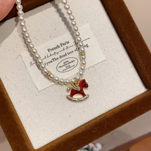 Detail view of a French-style pearl necklace with a red enamel rocking horse pendant.