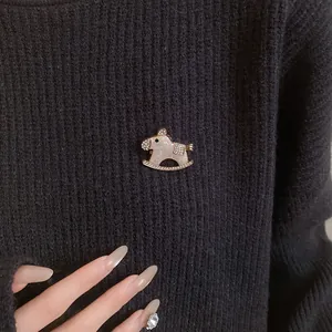 Close-up of a vintage rocking horse brooch with rhinestones on a black sweater.