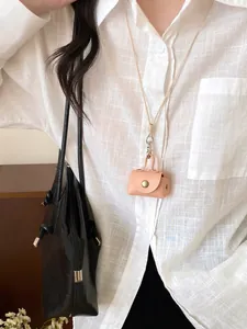 Detail view of a cute pink leather mini bag necklace pendant on a white linen shirt