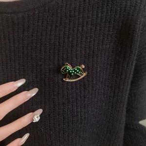 Close-up of a vintage green enamel rocking horse brooch with rhinestones on black knitwear