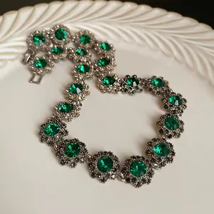 Dettaglio macro di una collana vintage a forma di fiore con gemme verdi brillanti.