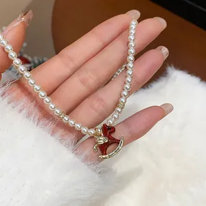 Detailed close-up showing white pearl necklace and red enamel rocking horse pendant