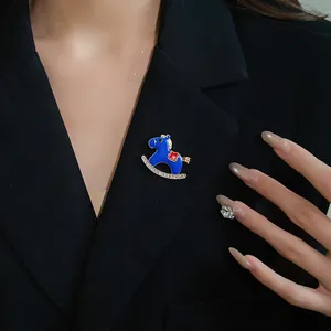 Close-up detail showing a blue enamel rocking horse brooch with rhinestones on a black blazer