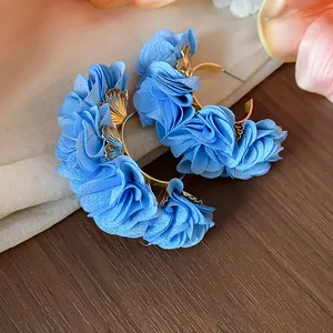 Close-up detail of light blue chiffon fabric flower C-shaped hoop earrings on wood.