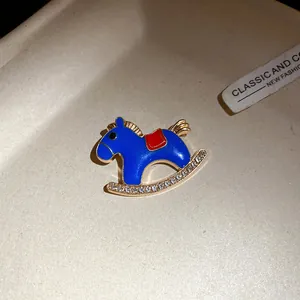 Close-up of a blue enamel rocking horse brooch with rhinestone details on a beige tray.