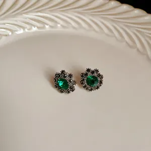 Dettaglio di orecchini a lobo vintage a fiore con cristalli verde smeraldo e accenti neri