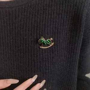 Detailed view of a green enamel rocking horse brooch with rhinestones on a sweater.
