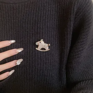 Detail shot of a vintage rocking horse brooch with rhinestones on a black knit sweater.