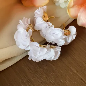 Close-up of white chiffon flower C-shape hoop earrings with gold leaf details