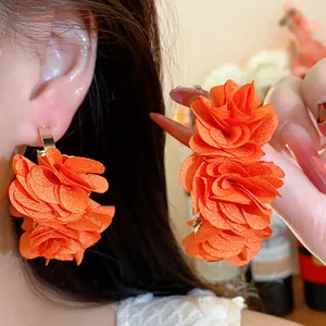 Close-up of vibrant orange chiffon flower earrings with C-shaped design and silver needles