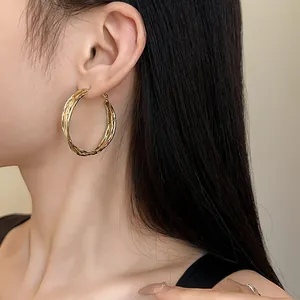 Detailed view of large golden intertwined geometric hoop earrings on an Asian female model