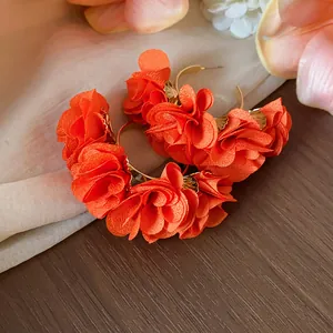 Close-up detail of vibrant orange chiffon flower C-shaped earrings on a silk background.