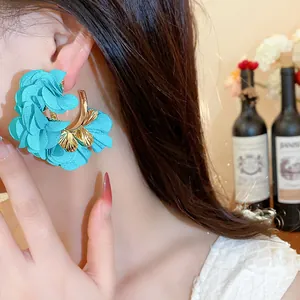 Close-up of turquoise chiffon flower C-shaped earrings on model in a lifestyle setting.