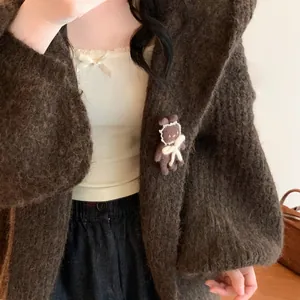 Close-up detail of a sweet brown flocked bear brooch with a white bow on a cardigan
