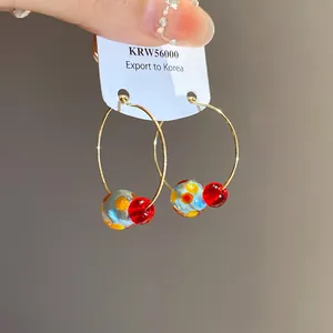 Close-up of gold hoop earrings with yellow-spotted blue beads and red beads