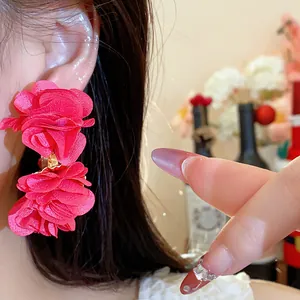 Detailed close-up of vibrant red chiffon fabric flower earrings worn on a model's ear