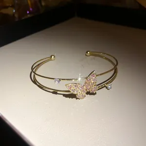 Close-up of elegant double-layer gold cuff bracelet with sparkling pink butterfly