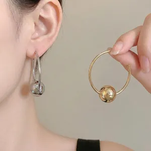 Minimalist silver and gold hoop earrings with a metallic ball charm worn by a model