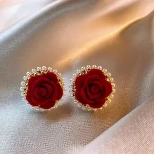 Dettaglio delle orecchini a lobo con rose rosse, bordo dorato e piccole perle