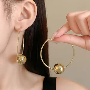 Detailed close-up view of oversized gold hoop earrings featuring a single polished metallic bead