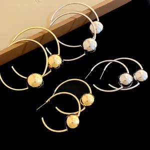 Close-up detail of minimalist gold and silver hoop earrings with spherical beads.