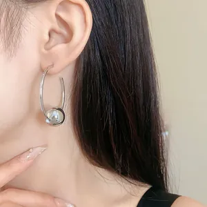 Close-up view of minimalist silver hoop earrings with a smooth metallic sphere charm