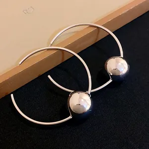 Close-up of minimalist silver hoop earrings featuring large polished metallic spheres