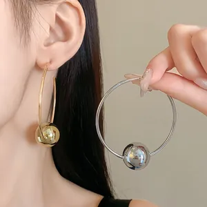 Detailed view of oversized silver and gold hoop earrings featuring a polished spherical bead