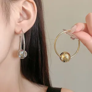 Close-up of minimalist hoop earrings with a metallic ball pendant in gold and silver